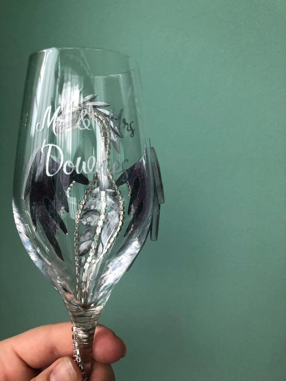 Handheld view of a sparkling wineglass adorned with iridescent dragon crystals against a calm turquoise backdrop.