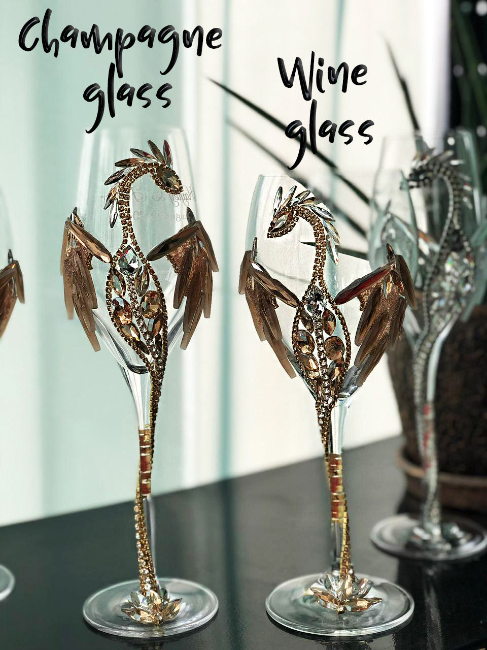 Close-up view of two ornate glasses: one labeled "Champagne glass" and the other labeled "Wine glass." Both glasses feature intricately designed stems resembling jeweled dragons with golden and silver accents against a serene backdrop