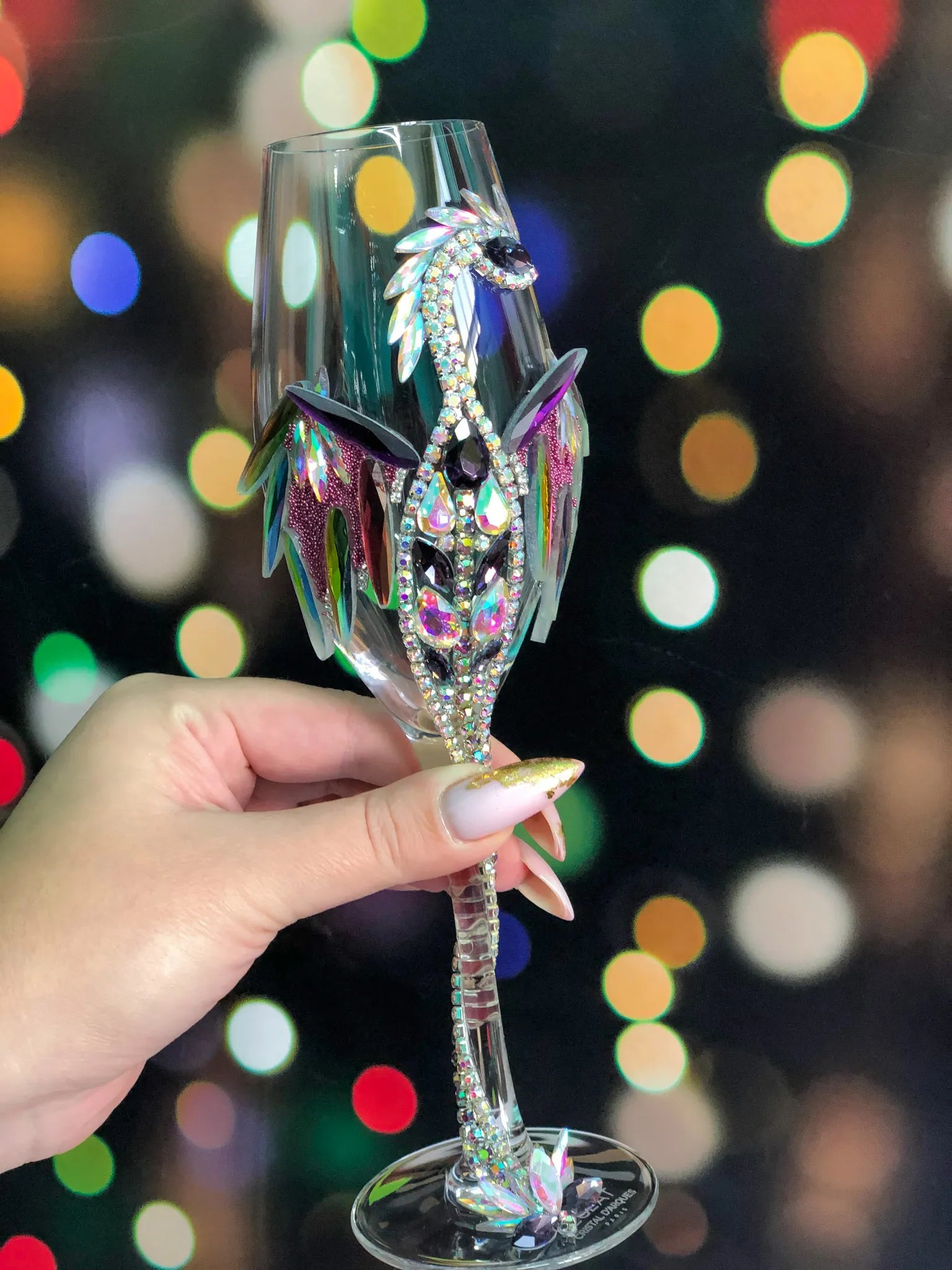 Glittering dragon-encrusted wineglass with multifaceted crystals capturing a dance of colorful city lights in the background