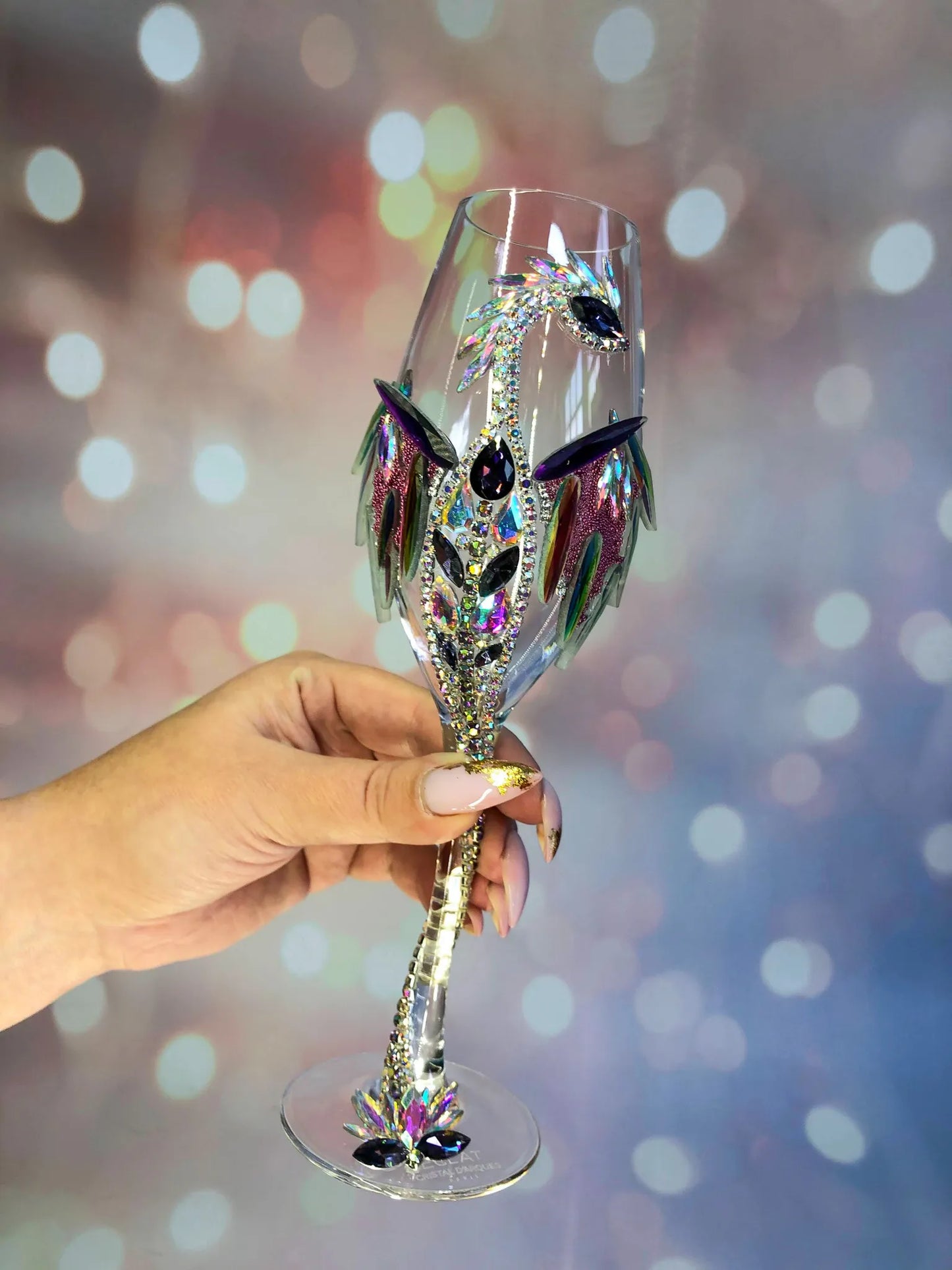 Elegant dragon wineglass held delicately in hand, showcasing its gleaming spiral stem and ornate crystal detailing against soft-focus lights.