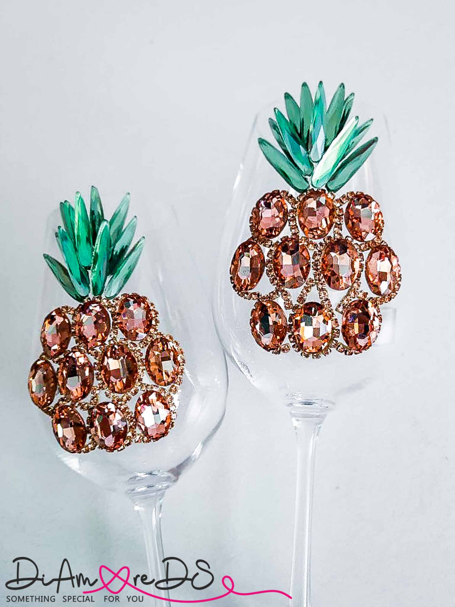 A pair of rose gold pineapple wine glasses set against a tropical backdrop, perfect for a beach-themed event.