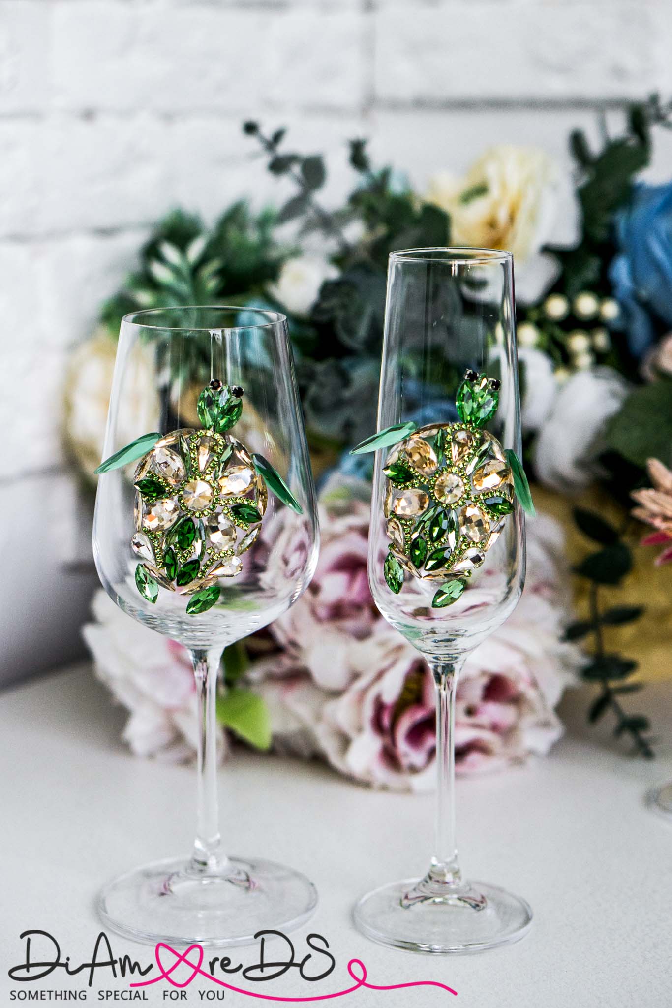 Pair of sea turtle wine glasses with exquisite green crystal decorations, set against a floral arrangement backdrop