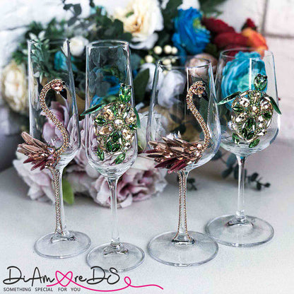 Assorted crystal champagne flutes with intricate flamingo and sea turtle jewel embellishments on a floral backdrop